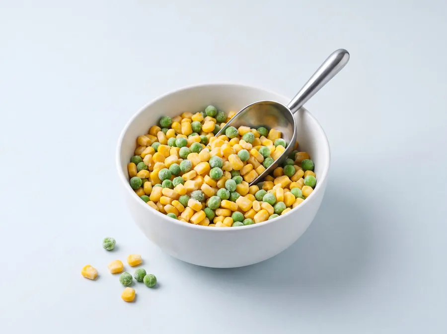 Frozen sweet corn and green peas mixed in a white bowl